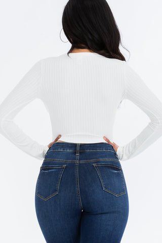 Back view of woman wearing white ribbed long sleeve snap button down crop top with denim jeans.