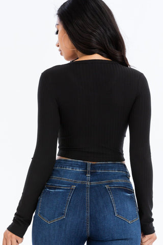 Back view of a woman wearing a black ribbed long sleeve snap button down crop top with high-waisted blue jeans.