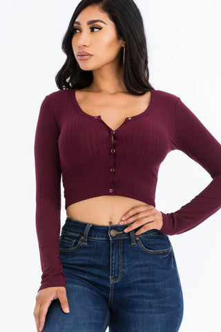 Woman wearing a ribbed long sleeve snap button down crop top in burgundy with high-waisted blue jeans, showcasing a stylish look.