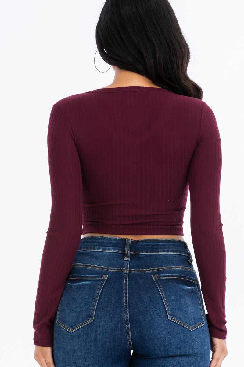 Back view of a model wearing a ribbed long sleeve snap button down crop top in burgundy, paired with high-rise blue jeans.