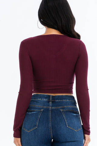 Back view of a model wearing a ribbed long sleeve snap button down crop top in burgundy, paired with high-rise blue jeans.