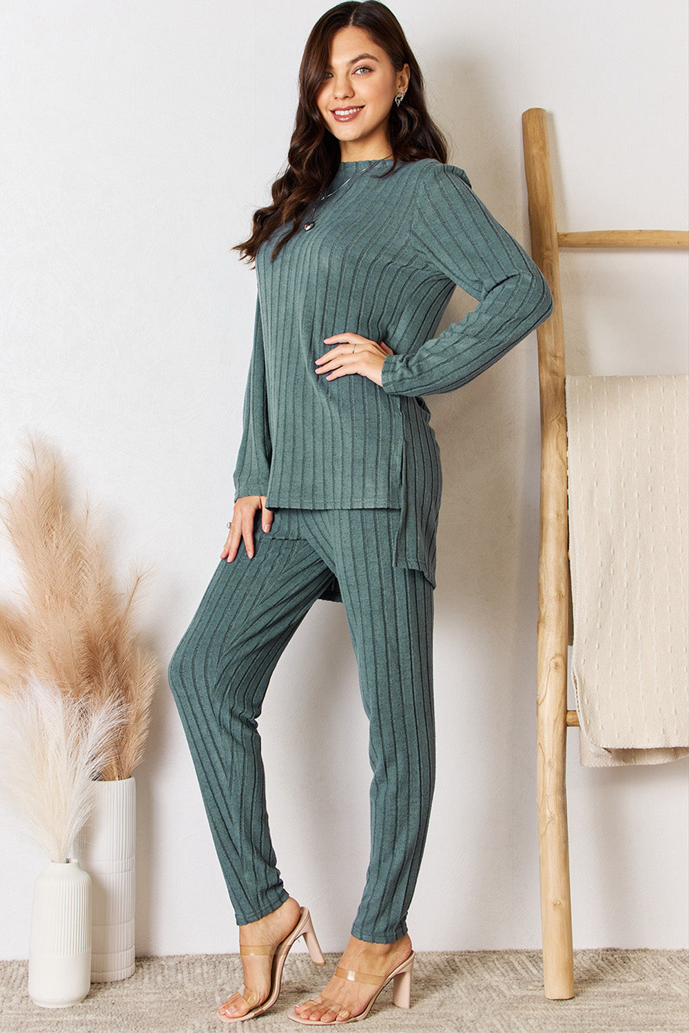 Woman wearing ribbed round neck high-low slit top and pants set in teal, featuring slightly stretchy fabric, standing in room decor.