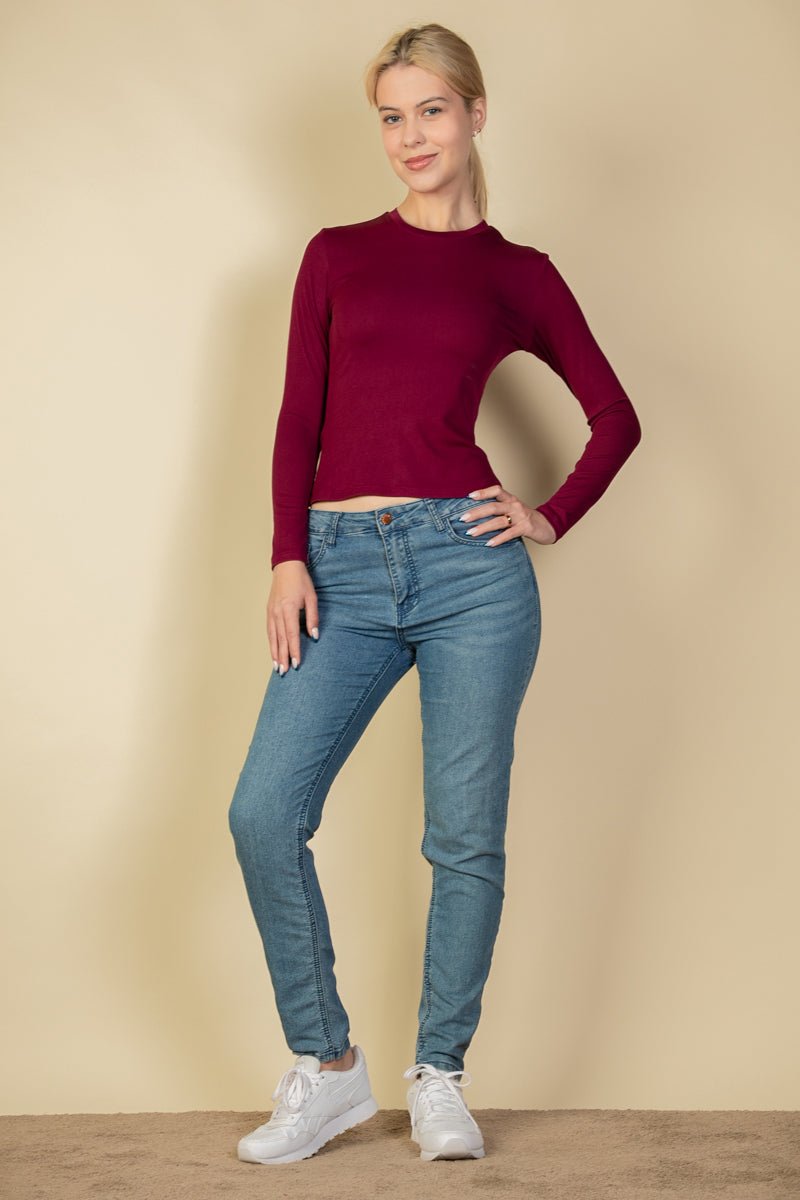 Model wearing ribbed round neck long sleeve top in burgundy with blue jeans and white sneakers, showcasing casual style fashion.