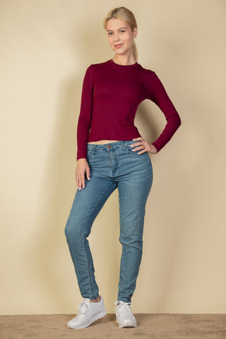 Model wearing ribbed round neck long sleeve top in burgundy with blue jeans and white sneakers, showcasing casual style fashion.