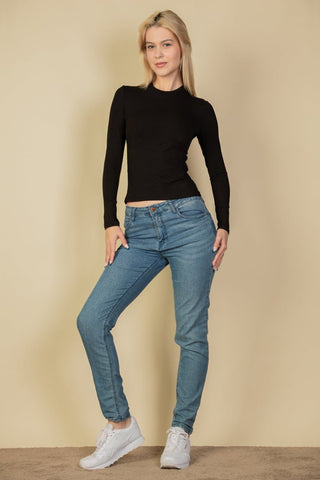 Model wearing ribbed round neck long sleeve top in black with blue jeans and sneakers.
