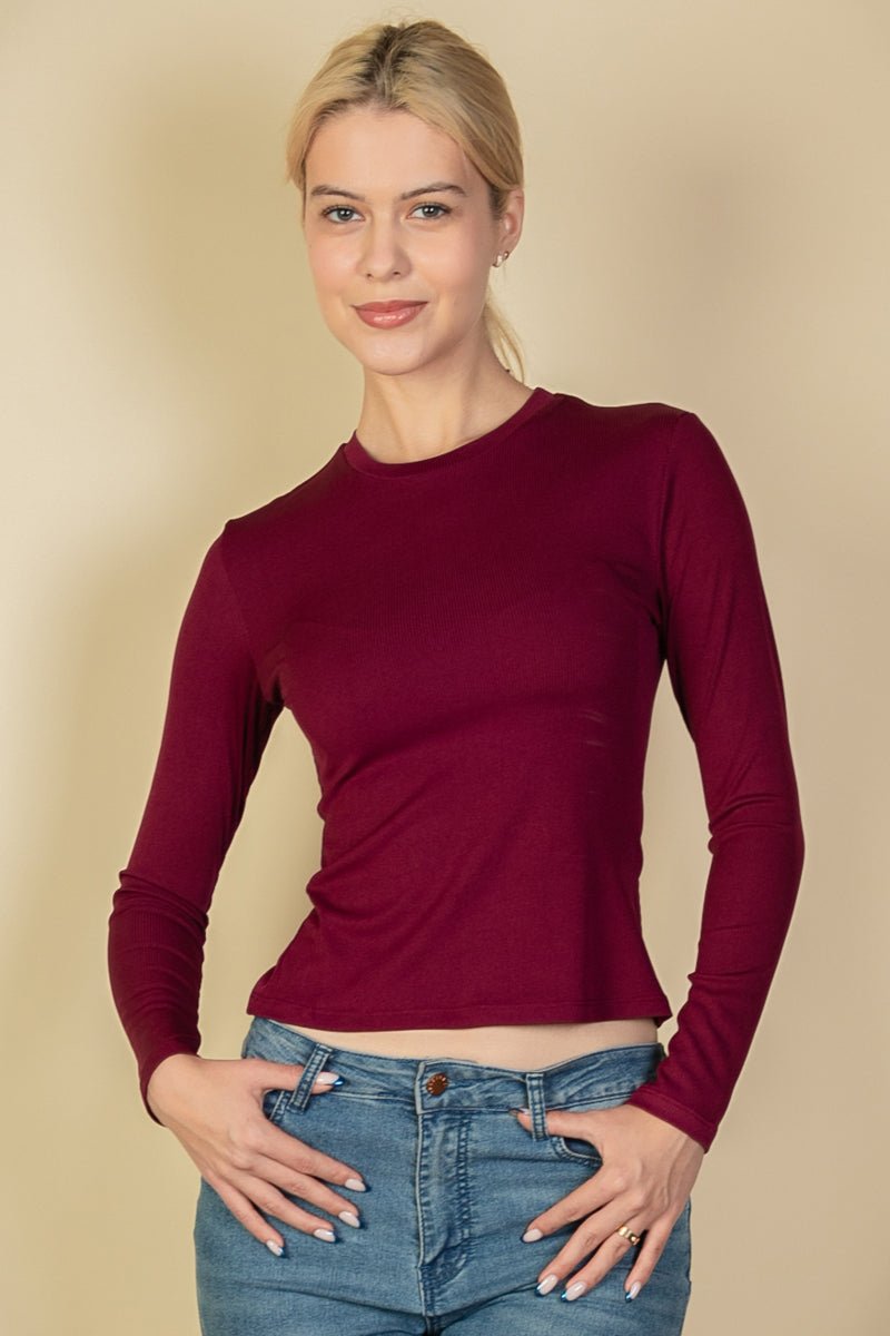 Woman wearing ribbed round neck long sleeve top in burgundy, soft stretch-knit fabric, paired with jeans.