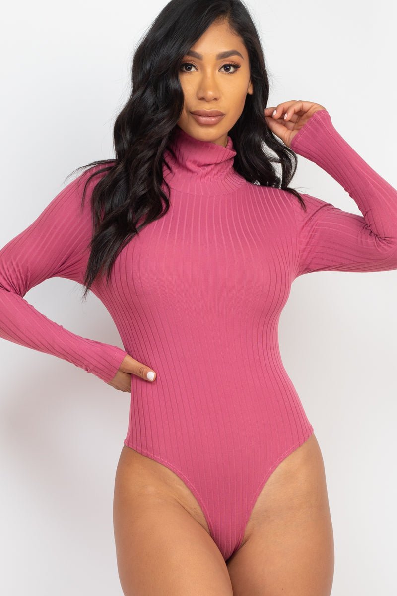 Model wearing a pink ribbed turtle neck long sleeve bodysuit, showcasing the soft, lightweight fabric with high stretch. Polyester and spandex blend.