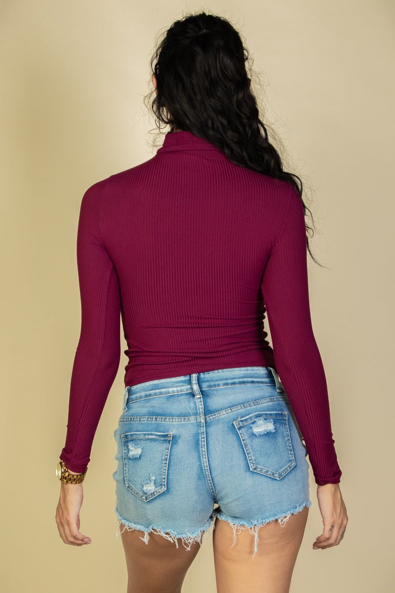 Back view of woman wearing ribbed burgundy turtleneck long sleeve top with light denim shorts, highlighting fitted and stylish design.