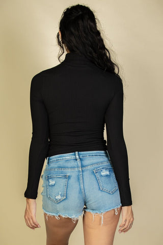 Back view of model in black ribbed turtleneck long sleeve top with high stretch, paired with denim shorts, showing lightweight fabric.