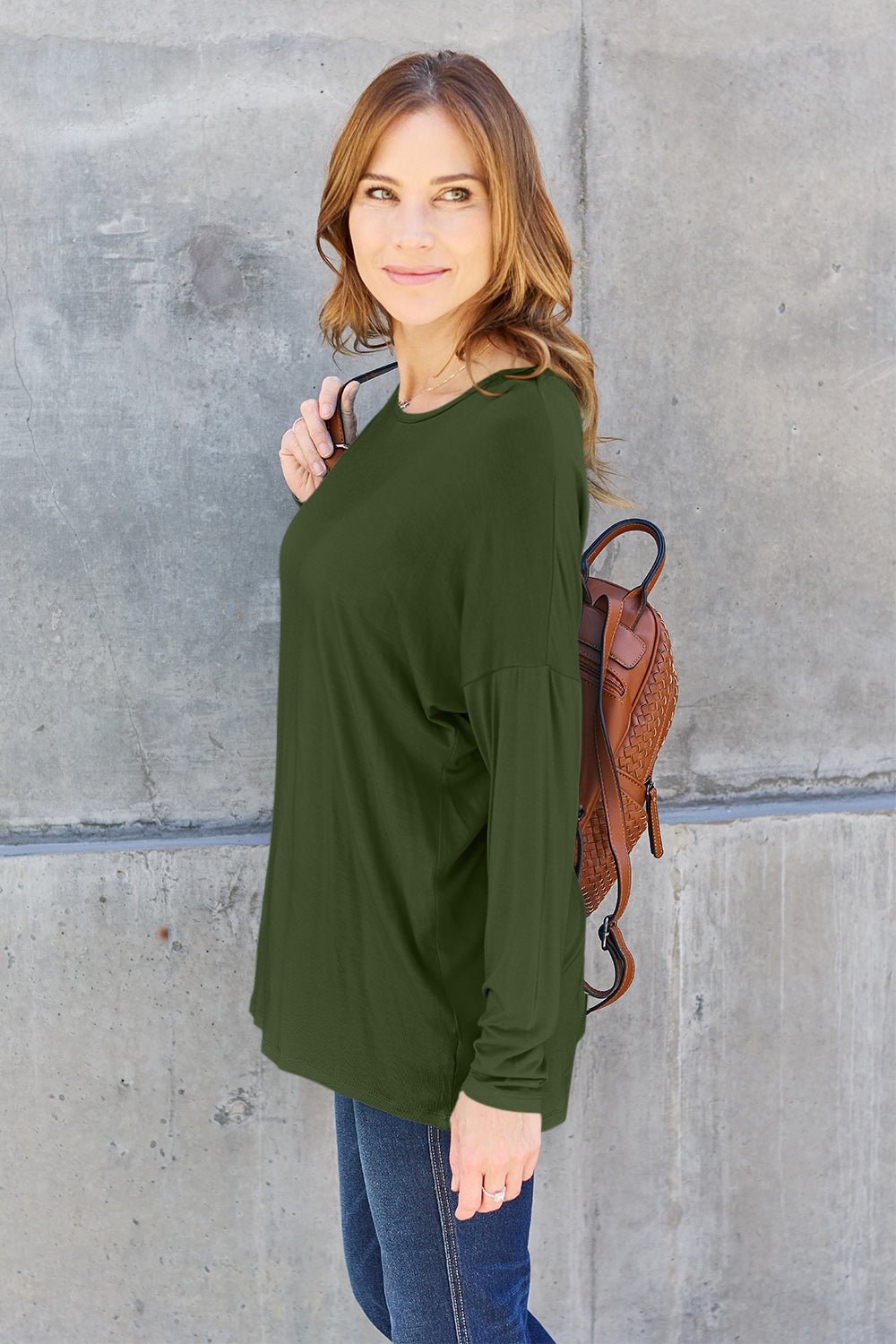 Woman wearing a round neck dropped shoulder t-shirt in green, paired with jeans, against a concrete background.