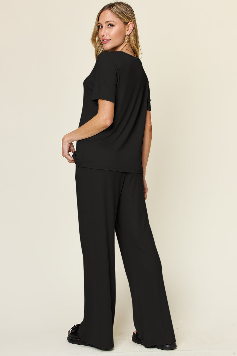 Woman wearing a black round neck short sleeve t-shirt and wide leg pants set, showcasing a basic style with slight stretch.