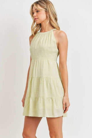 Woman wearing sage sleeveless round-neck dress with woven pompom textures and mini hemline.