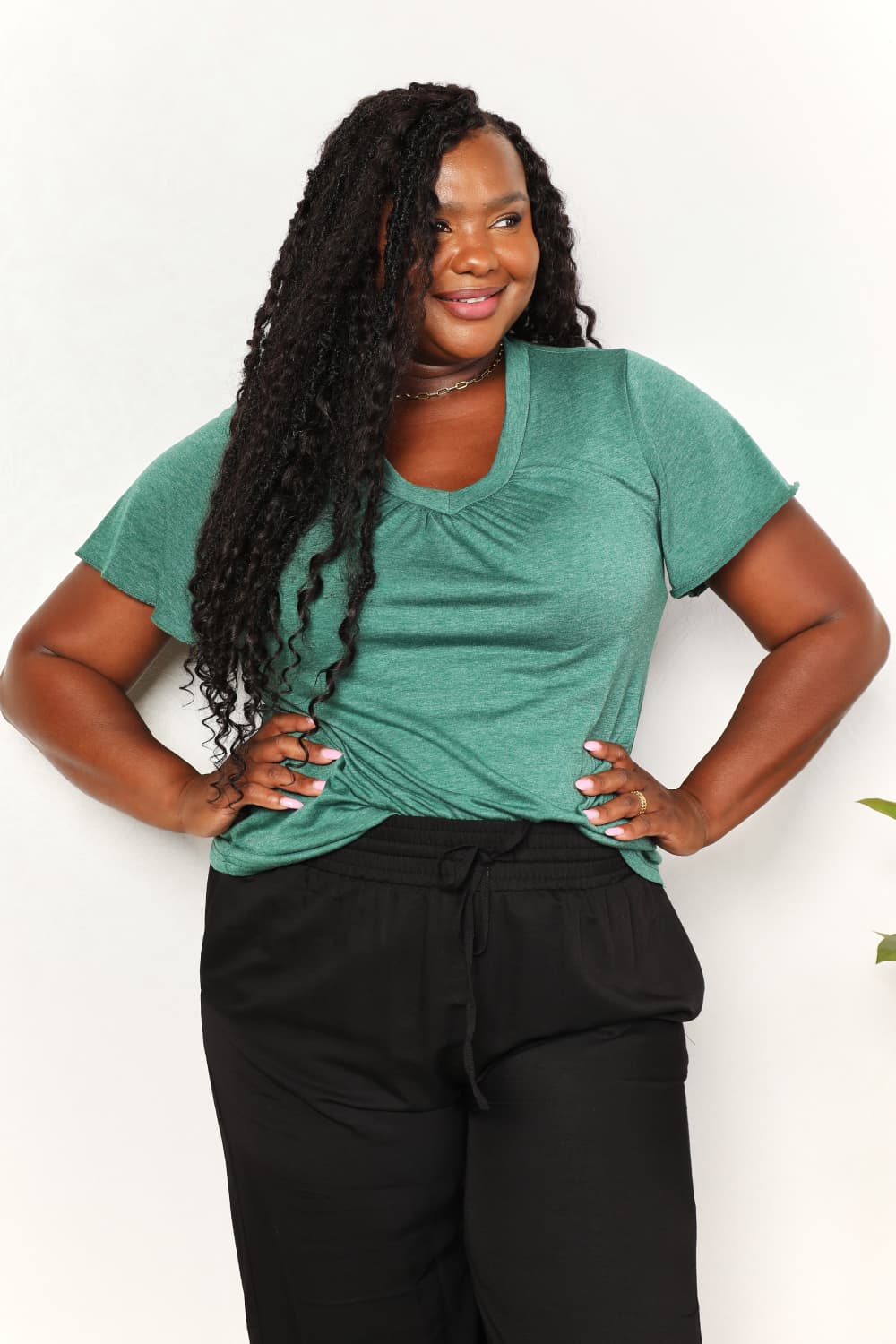 Woman wearing Double Take Ruched V-Neck T-Shirt with flutter sleeves and black pants, showcasing chic and comfortable style.