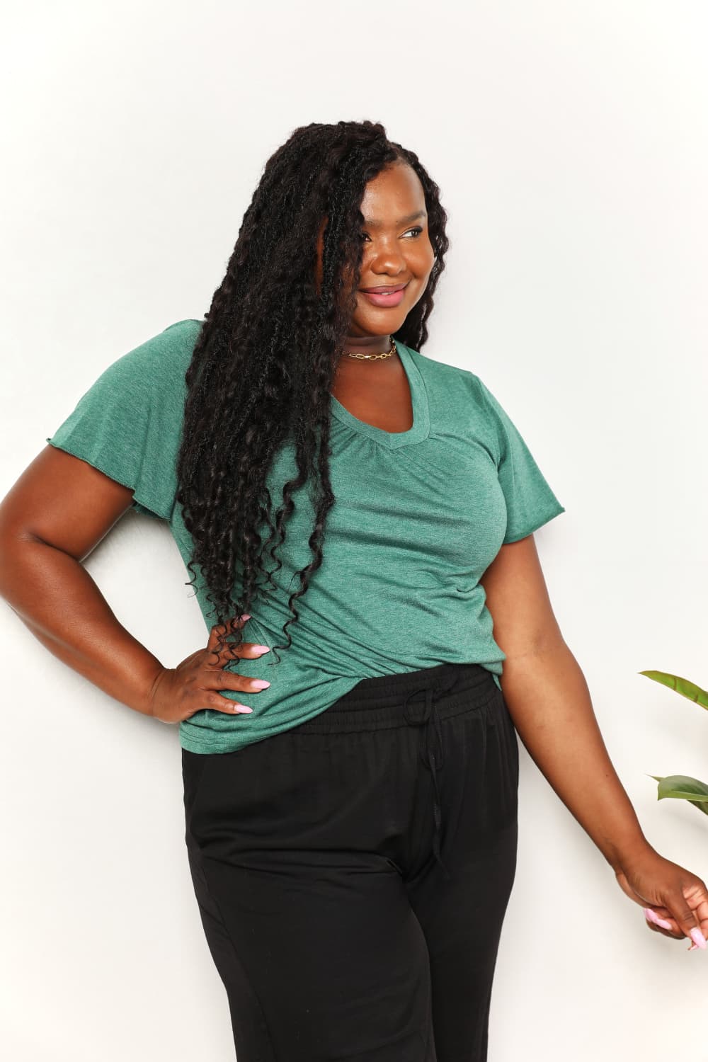 Woman wearing green ruched V-neck T-shirt and black pants, showcasing chic and comfortable fashion.