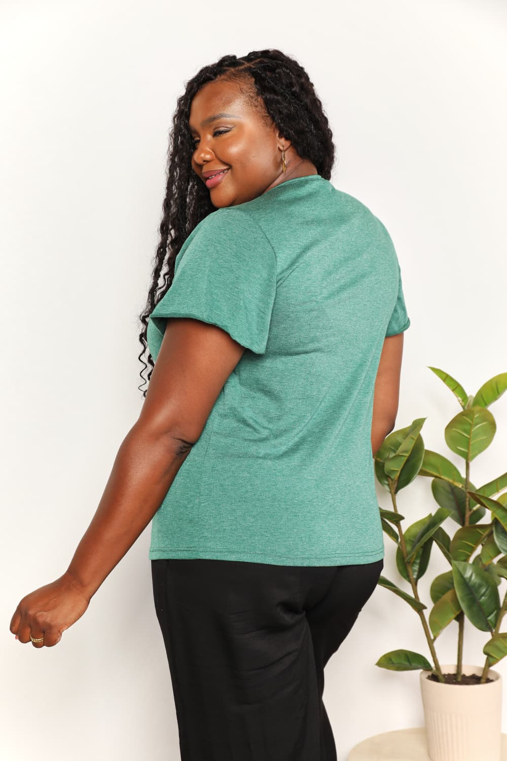 Woman wearing green ruched V-neck short sleeve T-shirt, showcasing back view with flutter sleeves.