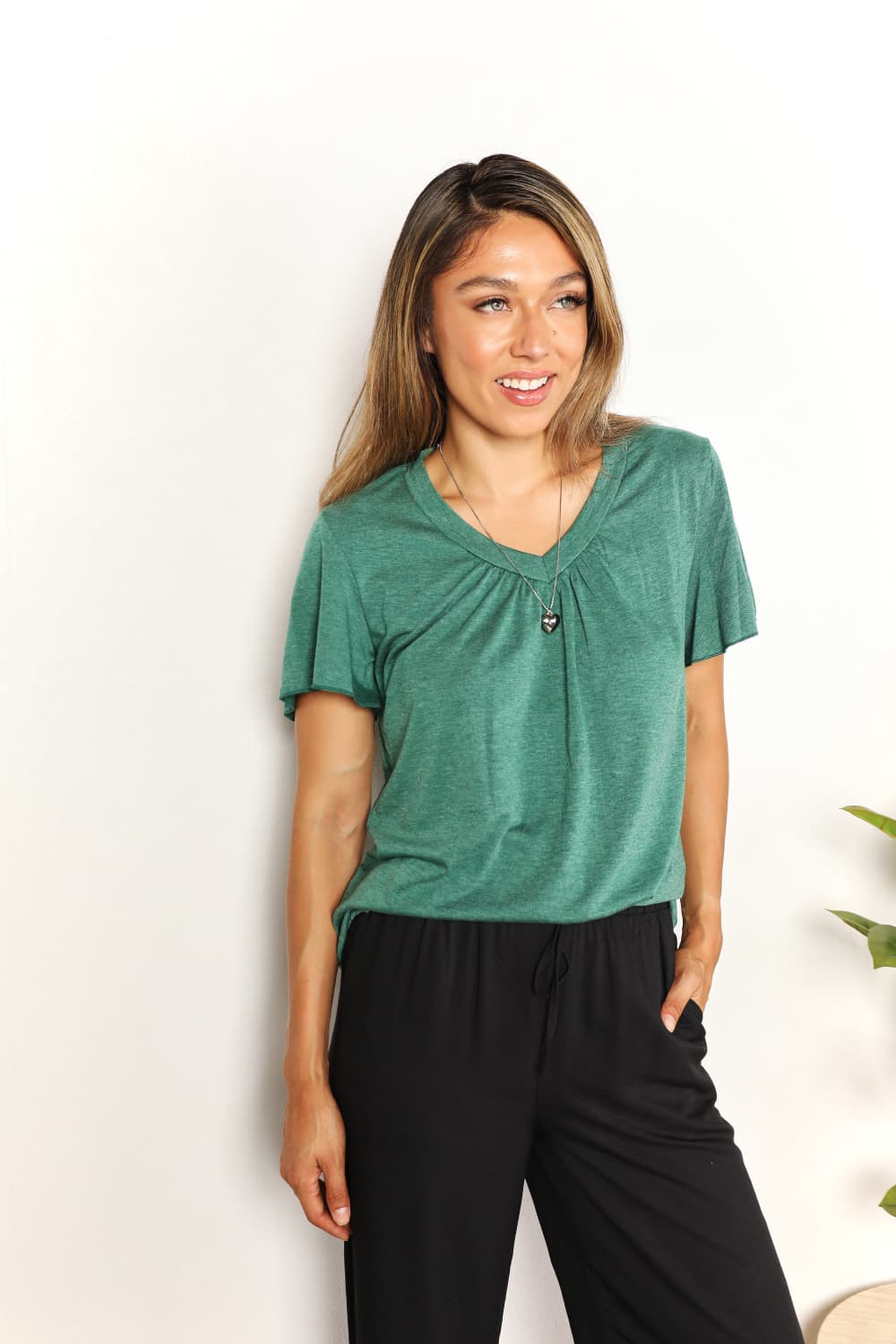 Woman wearing a green ruched V-neck short sleeve T-shirt, paired with black pants, showcasing a stylish and comfortable look.