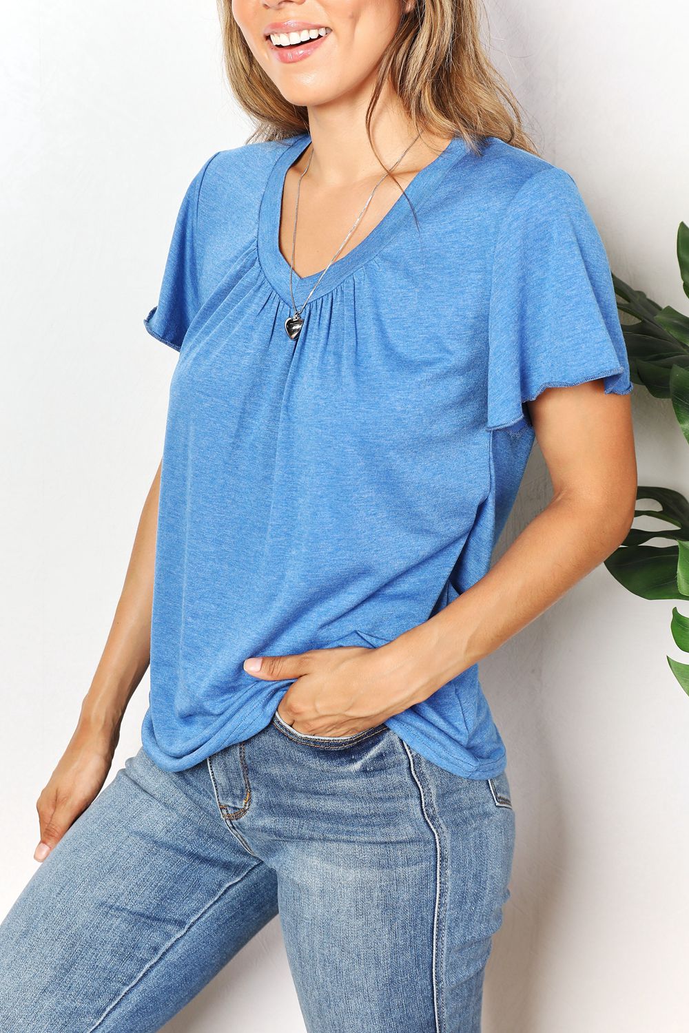 Woman wearing blue ruched V-neck short sleeve T-shirt with flutter sleeves, paired with jeans, showcasing a chic and comfortable look.