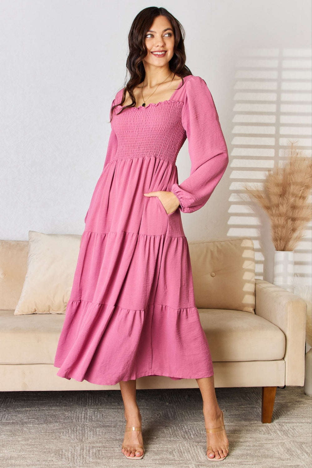 Pink ruffle trim smocked tiered dress with long sleeves, slightly stretchy polyester, modeled in a stylish setting.