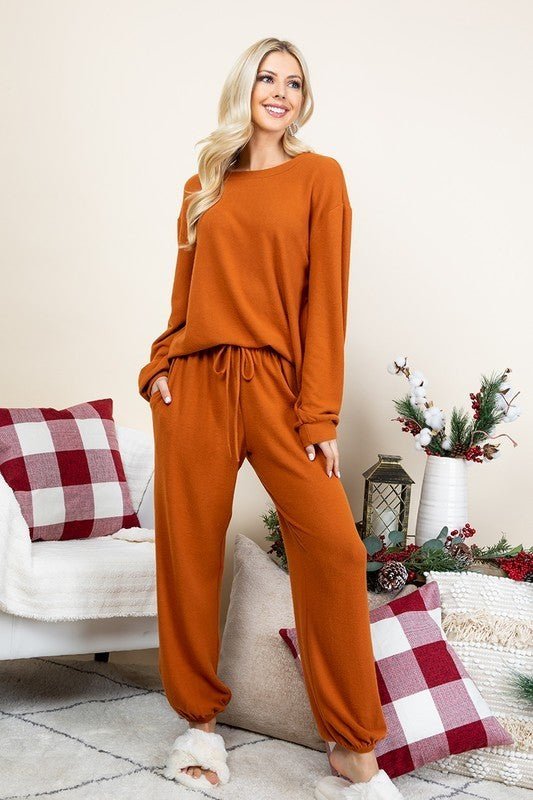 Woman wearing rust-colored fuzzy Hacci brush lounge set with round neck top and pants, standing in a cozy living room setting.