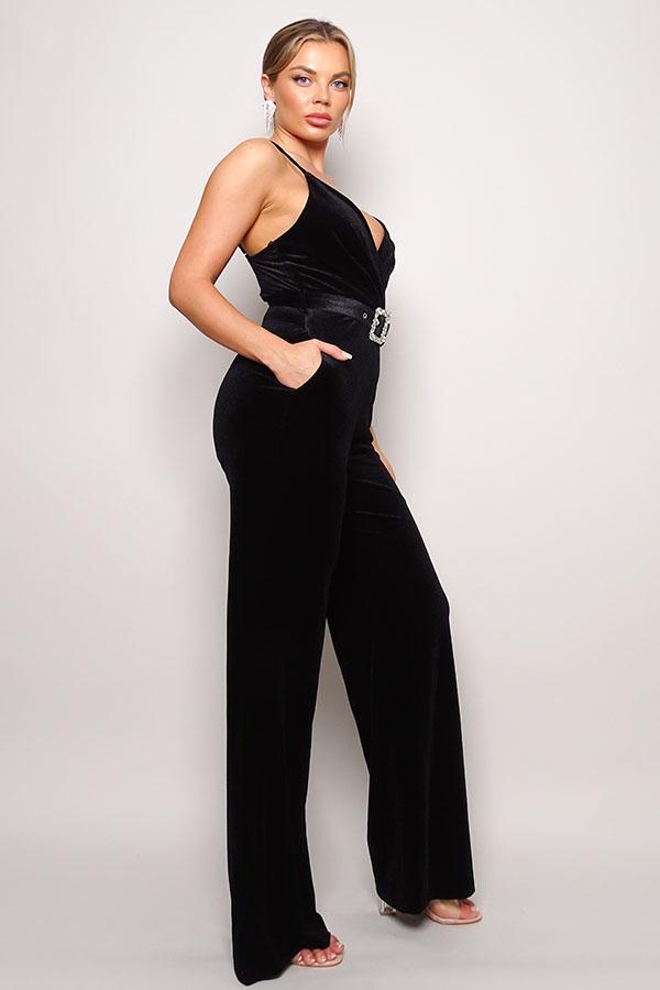 Woman wearing black velvet jumpsuit with rhinestone belt and crossover front design, featuring long pants and adjustable straps.