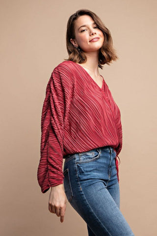 Woman wearing a burgundy satin pleated drawstring top with snap buttons and jeans, showcasing chic and contemporary fashion.