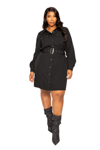 Plus-size model wearing a black satin effect belted jacket dress with button details and long sleeves, styled with black boots.