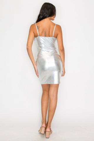 Woman wearing a silver foil mini dress with adjustable cami straps and scoop neck, showcasing a dazzling party look from the back.