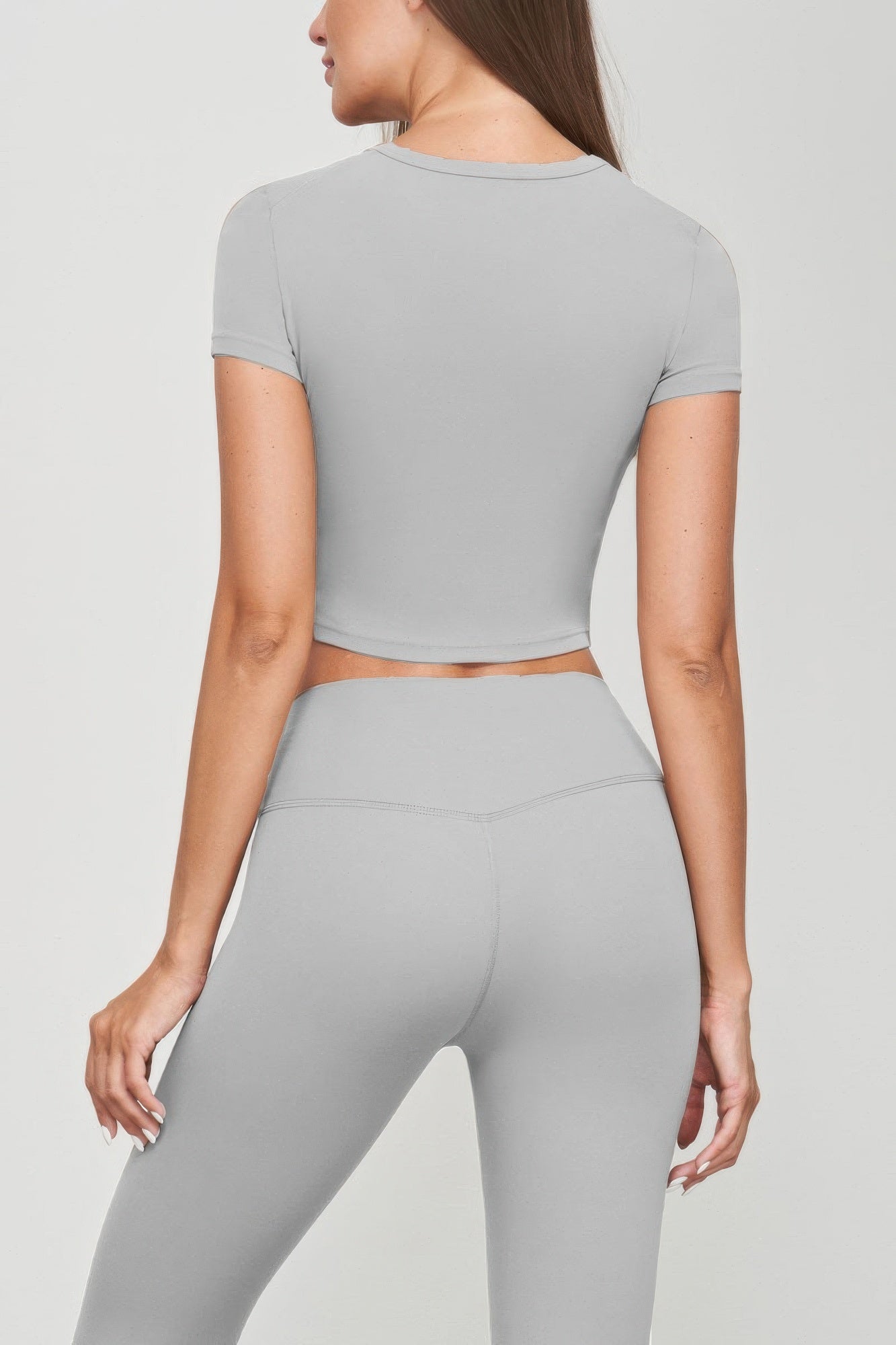 Back view of woman wearing grey seamless short sleeve crop tee and leggings, showcasing sleek, fitted silhouette. Perfect for casual wear.