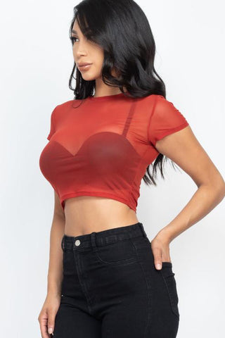 Woman wearing a red sexy mesh sheer short sleeve crop top, made of soft and lightweight fabric, paired with black pants. Fashionable and chic.