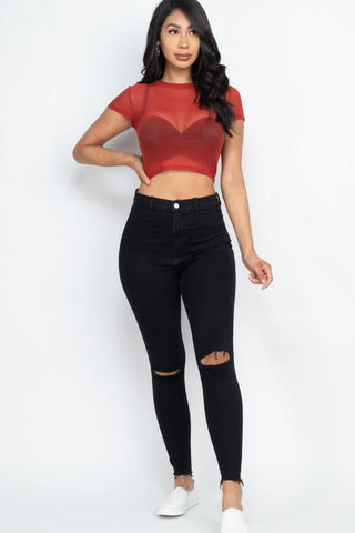 Woman wearing sexy mesh sheer short sleeve crop top in red with black ripped jeans and white sneakers.