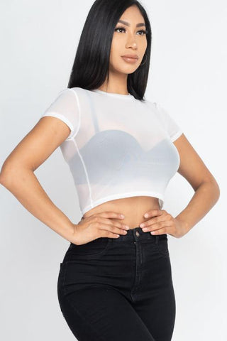Woman wearing sexy mesh sheer short sleeve crop top in white, paired with black jeans. Fashionable summer outfit.