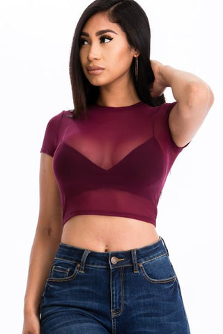 Woman wearing a sexy mesh sheer short sleeve crop top in maroon, paired with jeans. Fashionable summer outfit.