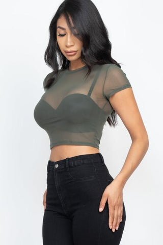 Woman wearing a sexy mesh sheer short sleeve crop top in dark green color with black jeans, highlighting trendy fashion style.