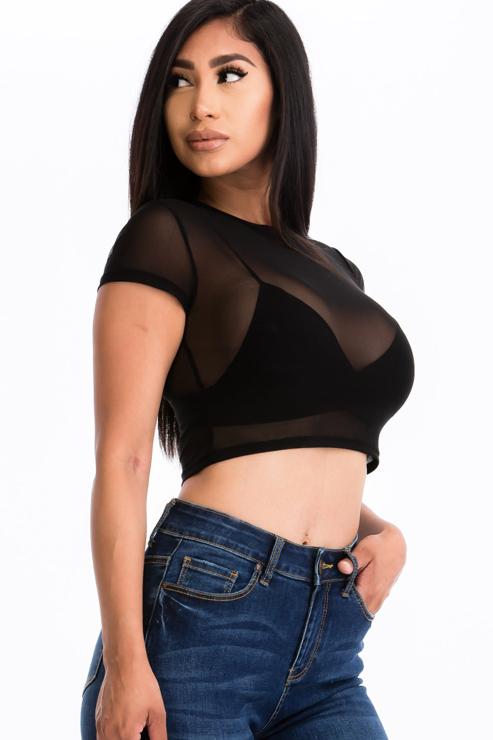 Woman wearing a sexy mesh sheer short sleeve crop top in black, paired with jeans. Fashionable and lightweight top for a chic look.