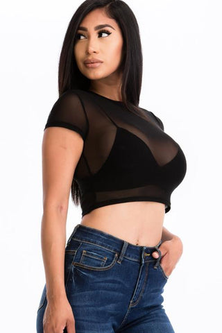 Woman wearing a sexy mesh sheer short sleeve crop top in black, paired with jeans. Fashionable and lightweight top for a chic look.
