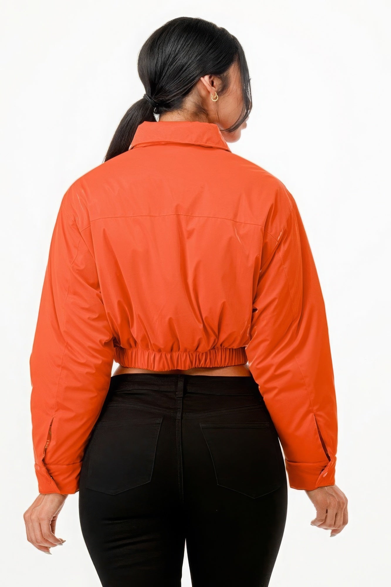 Woman wearing a shiny orange cropped puffer bomber jacket, rear view, showcasing the relaxed fit and elastic waistband.