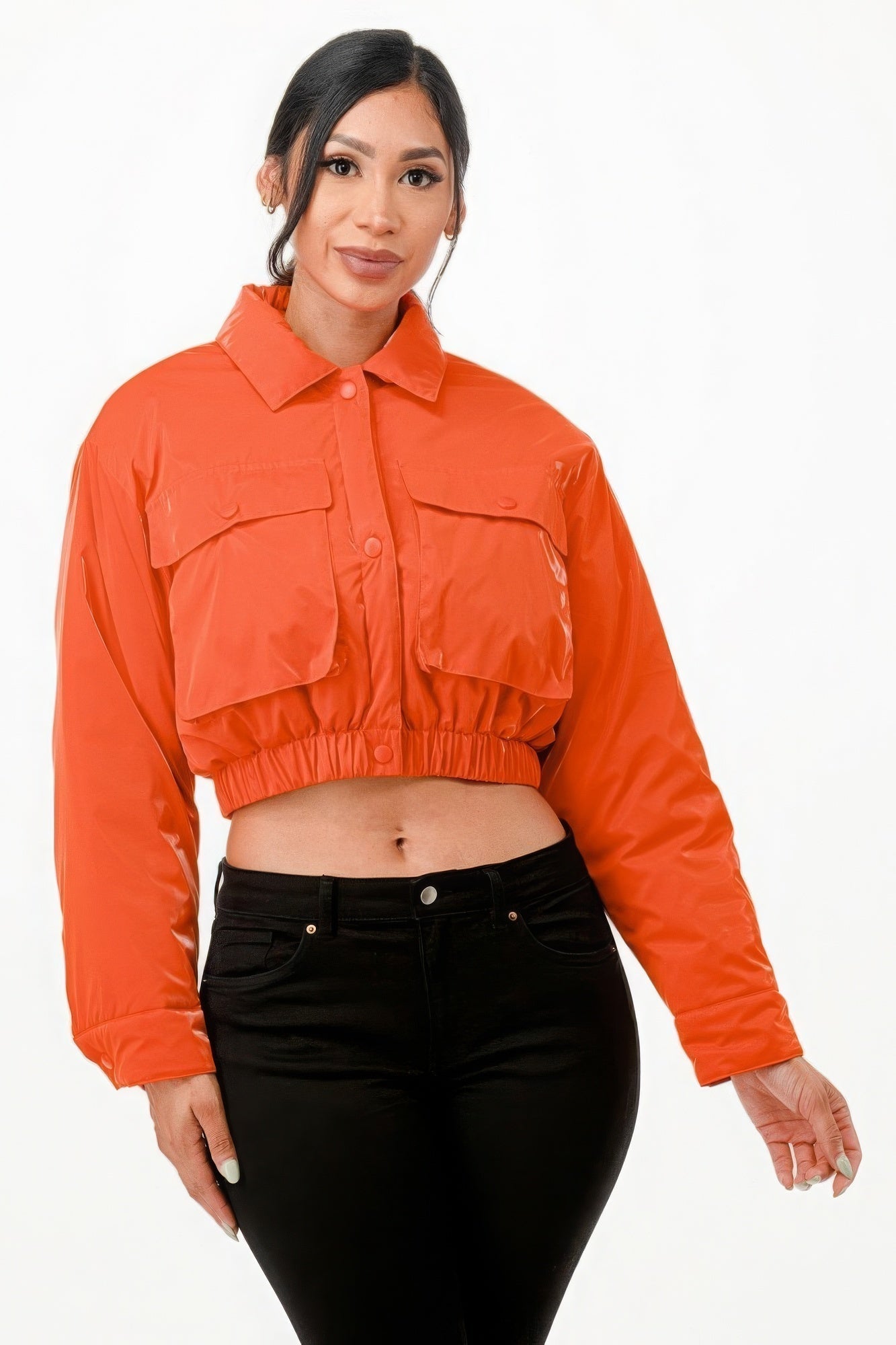 Woman wearing a bright orange cropped bomber jacket with two front pockets and snap button closure, showcasing a stylish and modern look.