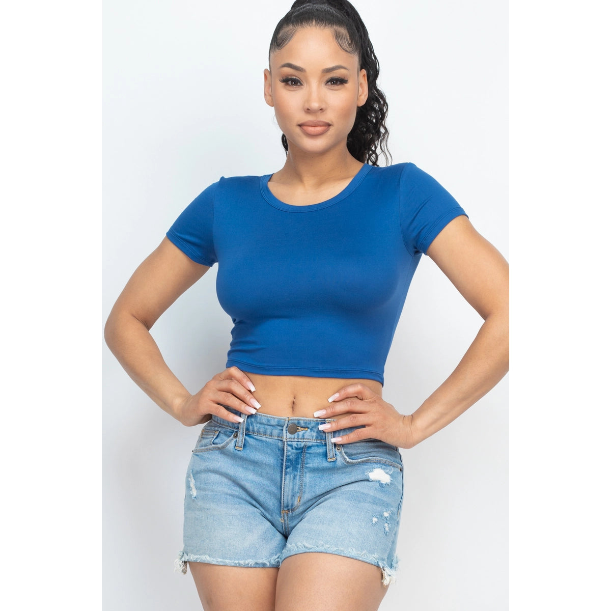 Woman in blue short sleeve roundneck crop top with denim shorts, showing casual summer fashion.