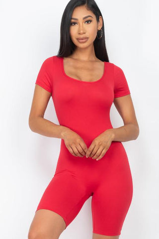 Woman wearing a red short sleeve scoop neck bodycon romper made of polyester and spandex, showcasing a tight yet comfortable fit.