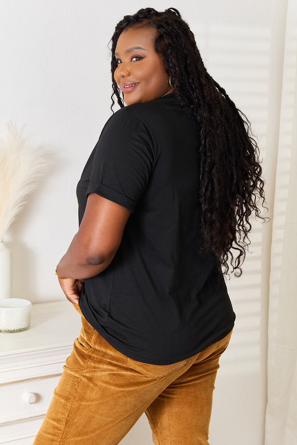 Woman wearing black "BE KIND" graphic round neck T-shirt with soft, stretchy fabric, paired with brown pants.