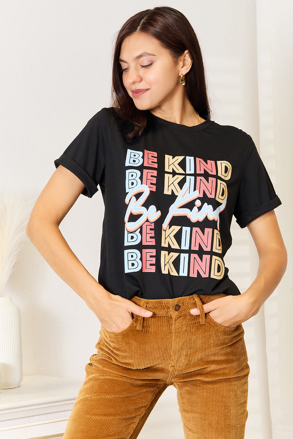 Woman wearing a black "BE KIND" graphic round neck T-shirt styled with brown corduroy pants.