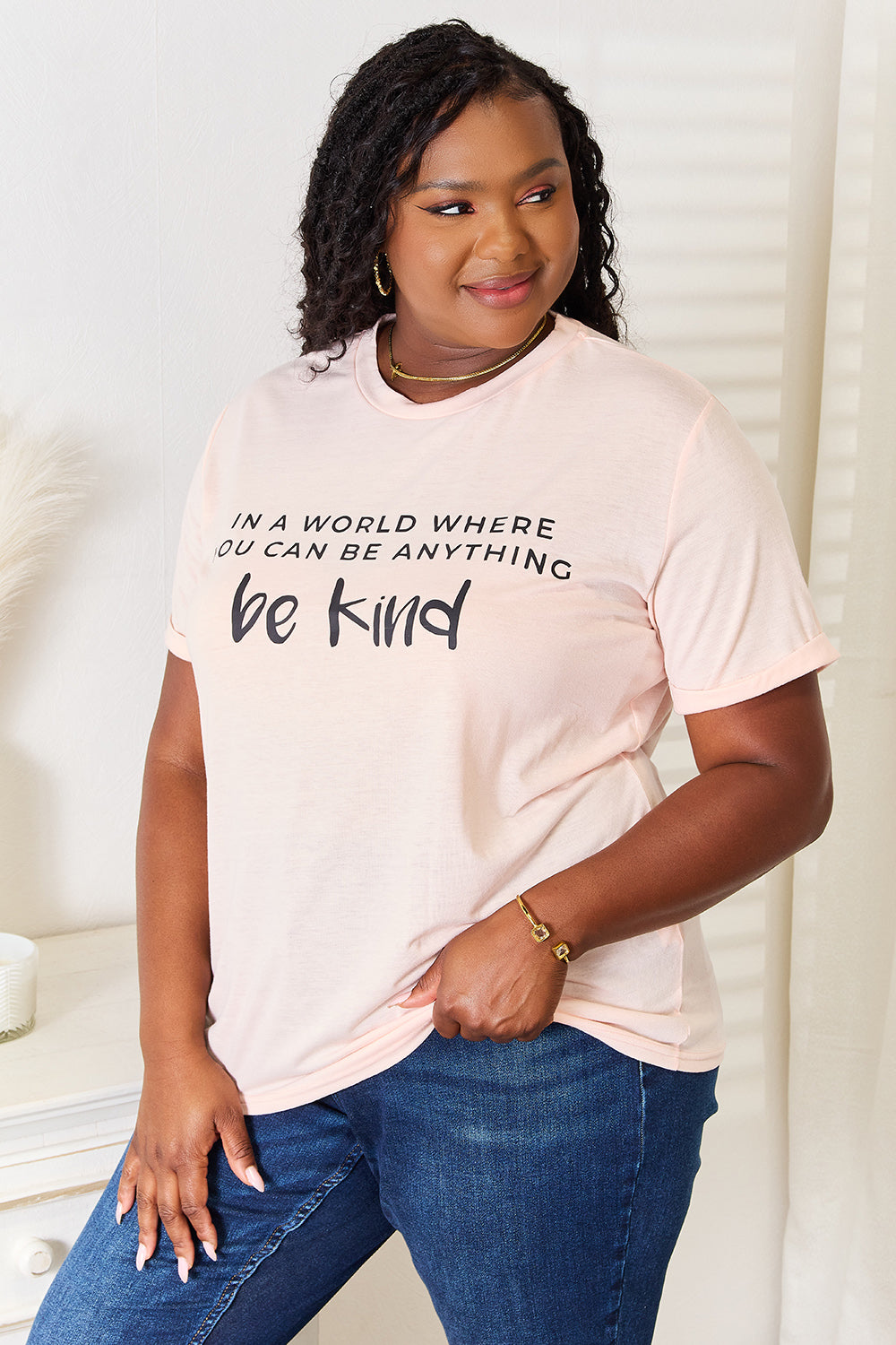 Woman wearing slogan graphic cuffed t-shirt with "be kind" design, paired with jeans, showcasing timeless, versatile style.