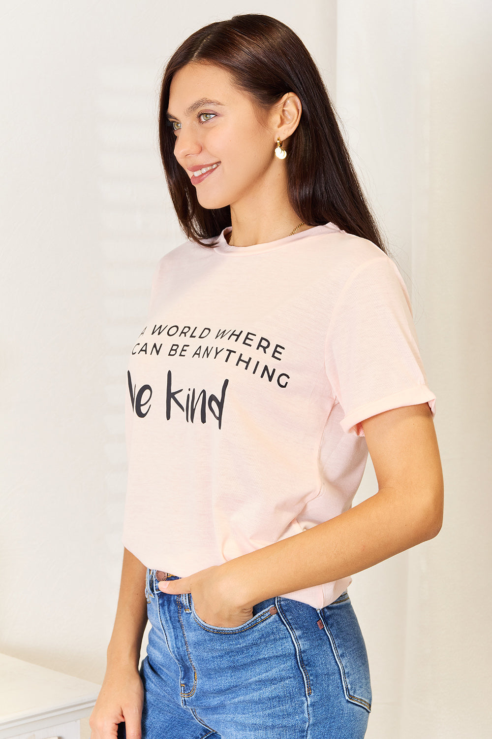 Woman wearing a slogan graphic cuffed T-shirt with "Be Kind" text, paired with blue jeans.