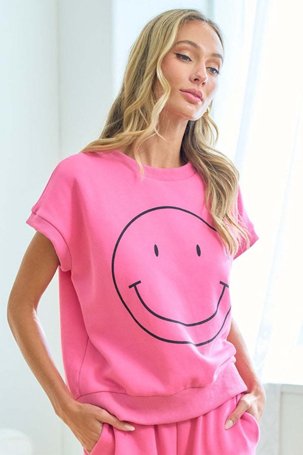 Woman wearing a pink Smile T-Shirt with a happy face design, drop shoulder style, in a chic and versatile wardrobe essential look.