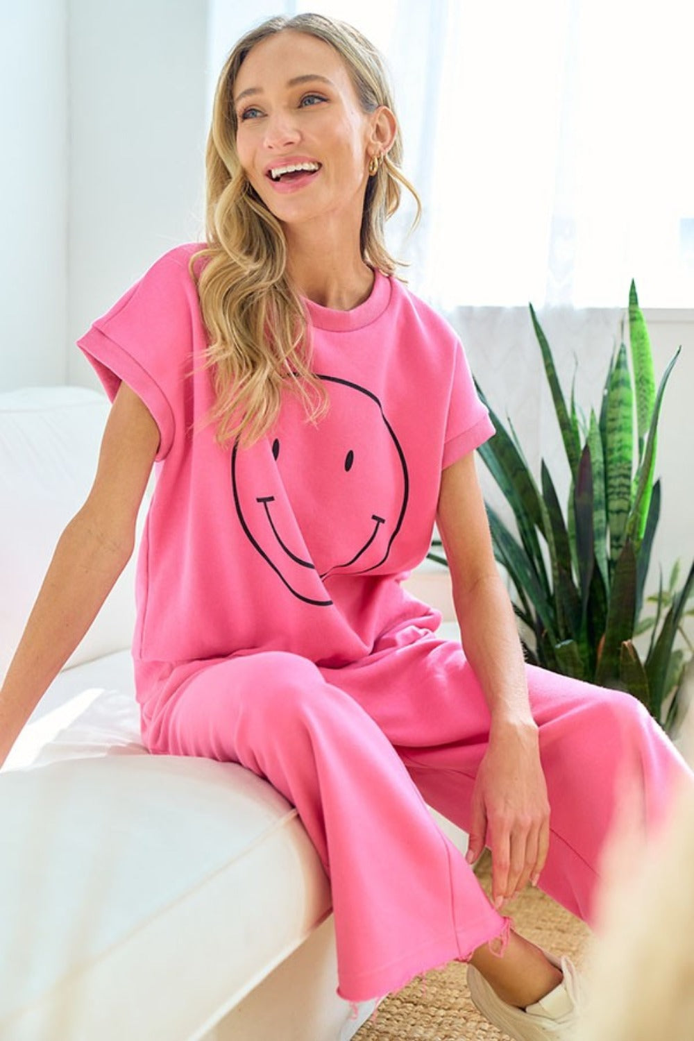 Woman wearing pink Smile T-Shirt Face Drop Shoulder lounging indoors, showcasing casual chic style with a smile design.