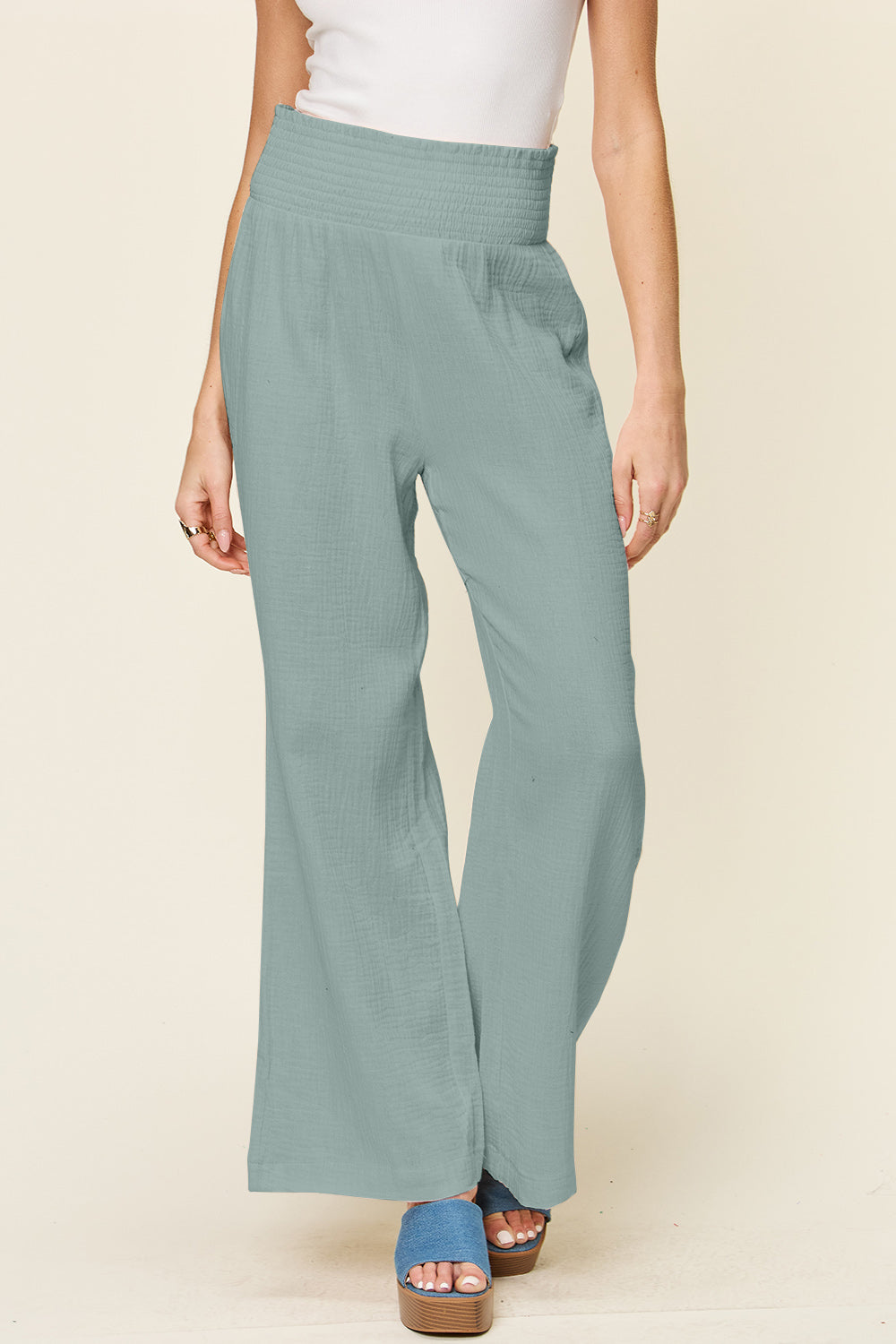 Woman wearing texture smocked waist wide leg pants in 100% cotton, pastel green color, paired with blue sandals.