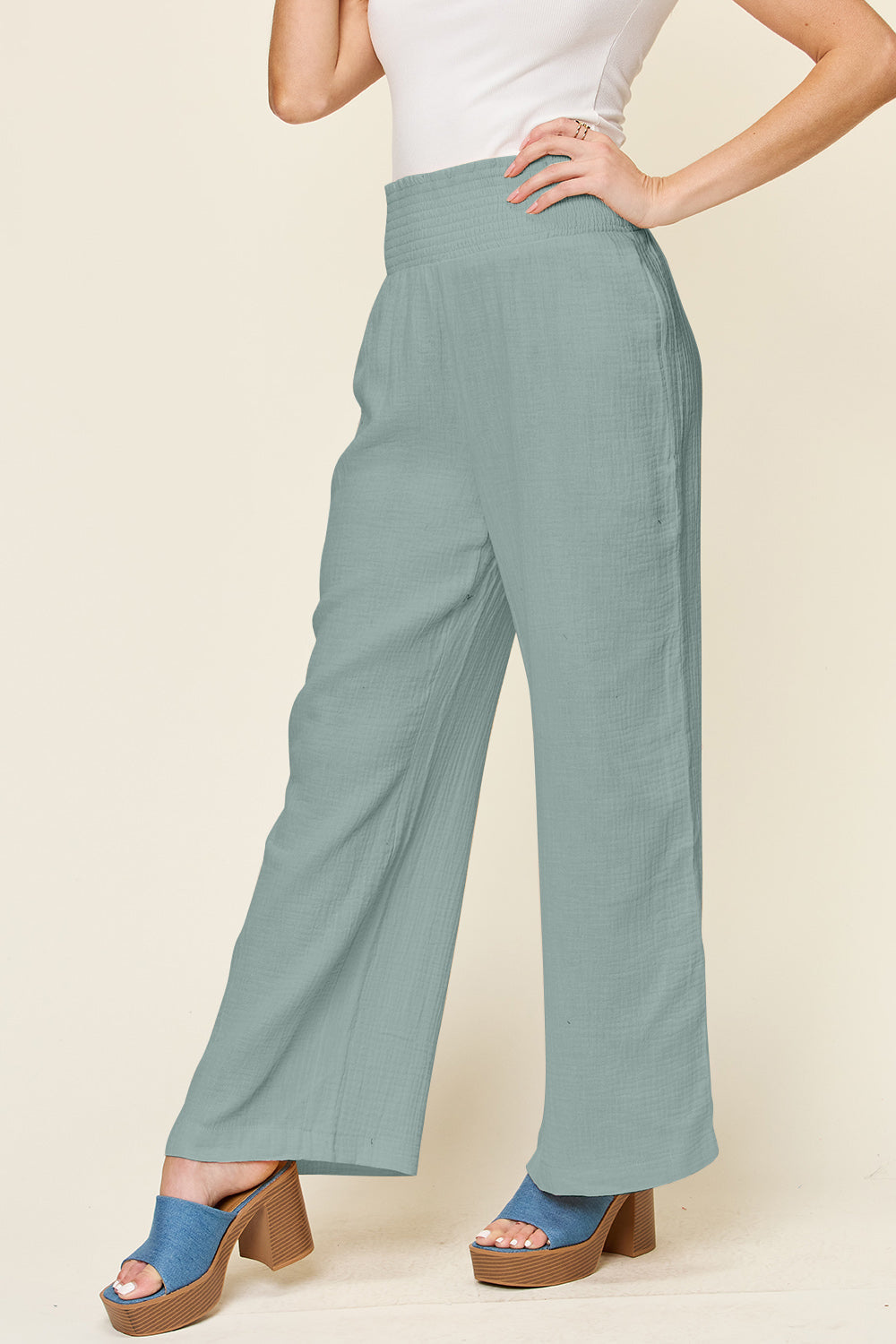 Woman wearing green smocked waist wide leg cotton pants with blue heels.