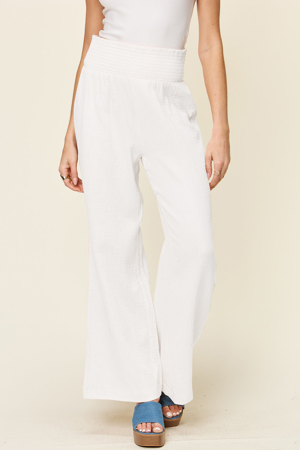 Woman wearing white texture smocked waist wide leg pants made of 100% cotton, paired with blue shoes.