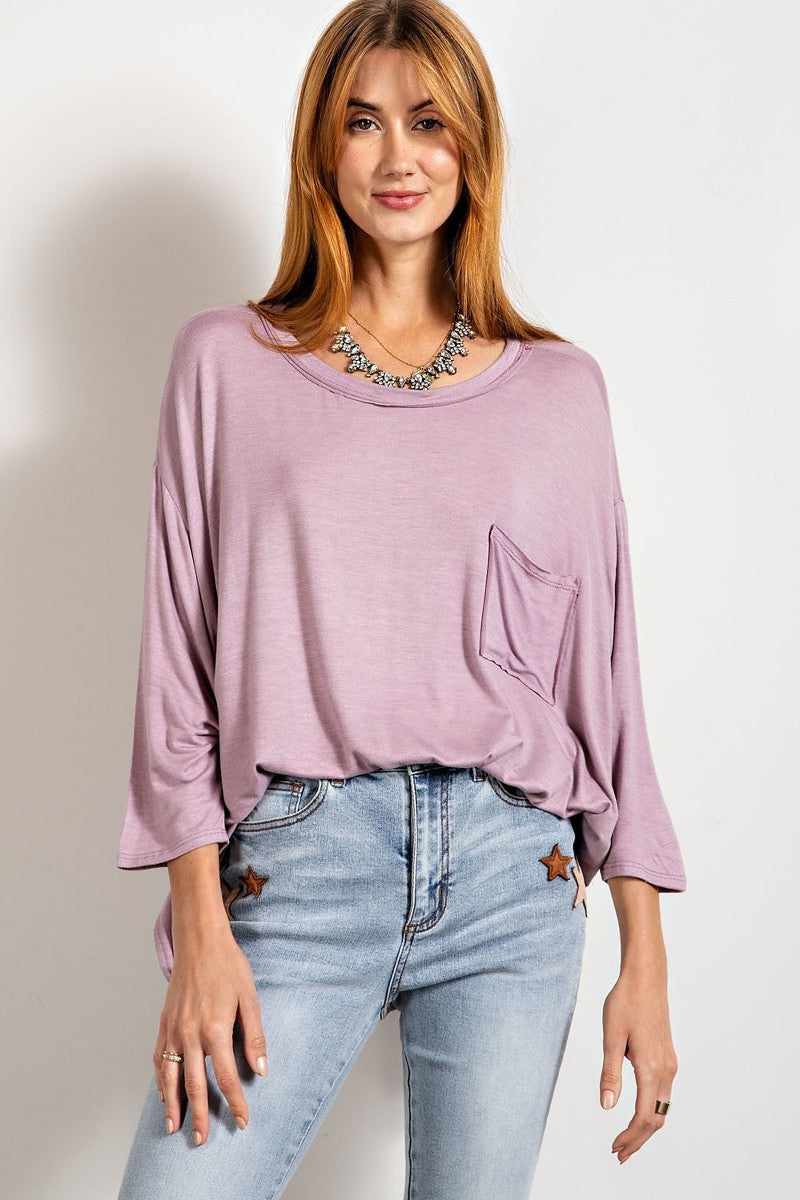 Woman wearing dusty lavender rounded neckline 3/4 sleeves washed top with chest patch pocket and side slits, paired with jeans.