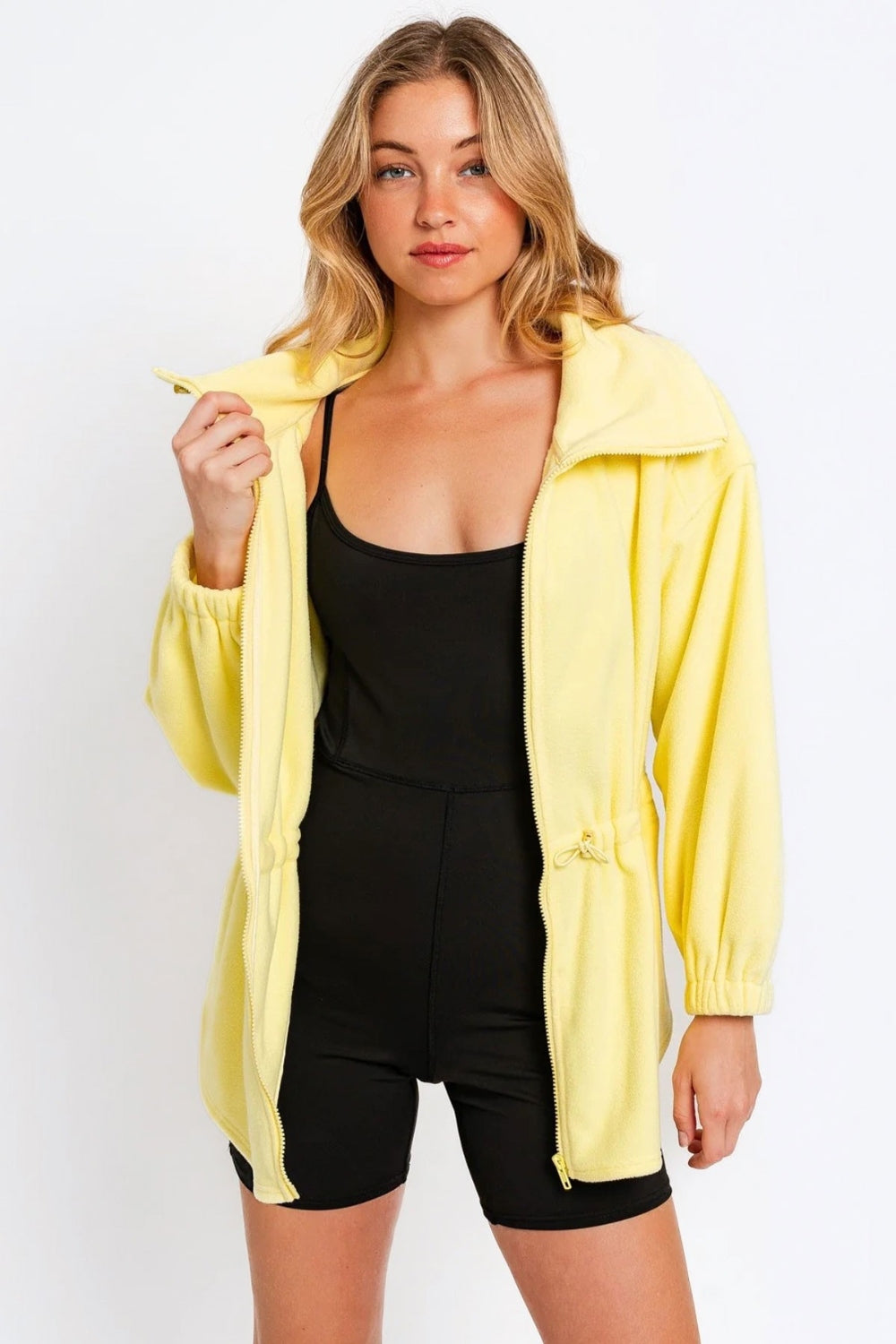 Yellow zip up waist drawstring soft fleece jacket over black outfit worn by model.